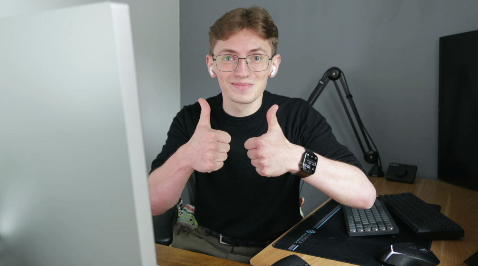 Young man with glasses giving double thumbs up at desk.